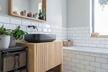 Modern bathroom sink in industrial interior with white tile on the wall and wooden mirror and black ceramic wash basin.