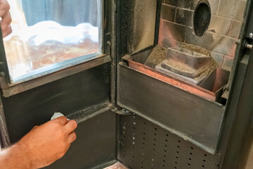 Close-up of a man cleaning the soot produced by the pellet stove in his living room, sustainable...