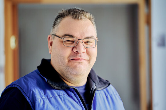 Face of large European man, 47 years old, wearing prescription glasses and smiling slyly.