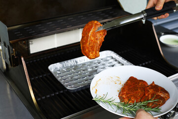 Raw meat is put on the grill before cooking, a man cooks a steak at home on the grill with rosemary