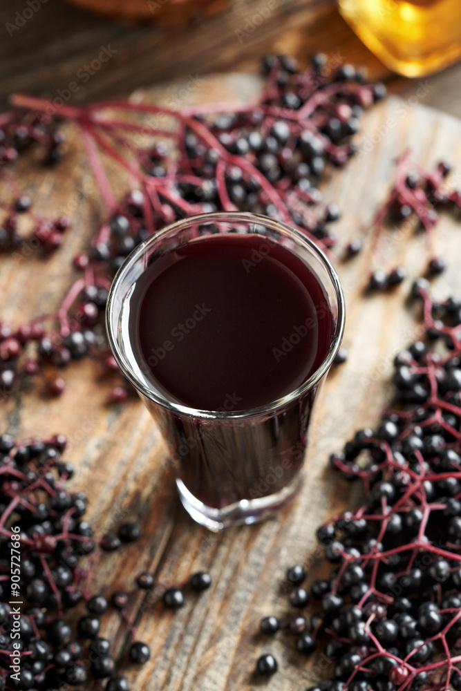 Wall mural Black elderberry syrup in a glass cup with fresh berries