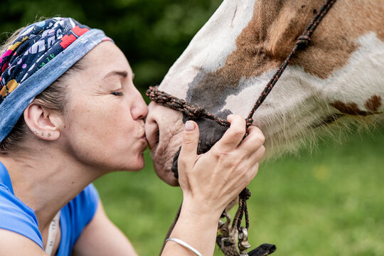 Woman kissing a painted horse in a lush green field - Powered by Adobe