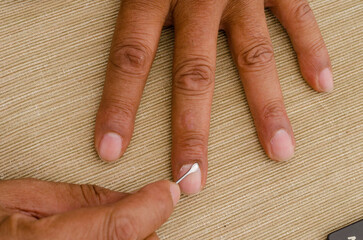 A person is using a cuticle remover file to clean their nails
