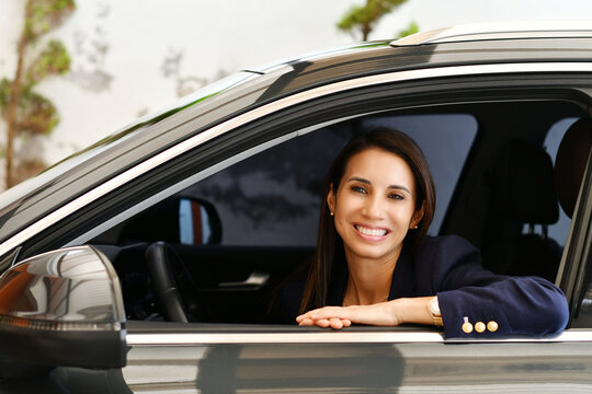 Mujer joven adulta feliz por la compra de su auto nuevo, sonriente en la ventana del veh&iacute;culo nuevo.