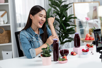 Smiling young beautiful Asian reviewing tasty mixed strawberry and cherry juice detox drinks,...