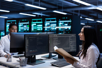 Team of engineers in data center checking emergency procedures documents to ensure system failure...