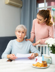 Senior woman felling upset about bills payment trouble. Daughter trying to comfort her.