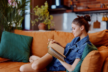 Obraz premium Young woman enjoying a relaxing moment reading a book on a comfortable orange couch in cozy living room