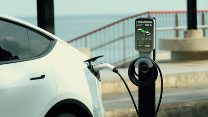 Electric car recharging battery at outdoor EV charging station for road trip or car traveling by...