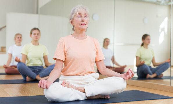 Group of people of different ages sitting in lotus position practicing meditation in yoga class - Powered by Adobe