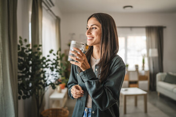 Portrait of adult women stand, hold glass of water look out the window