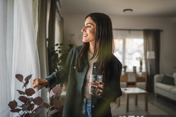 Portrait of adult women stand, hold glass of water look out the window