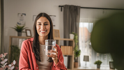 Portrait of adult young women stand and hold glass of water at home
