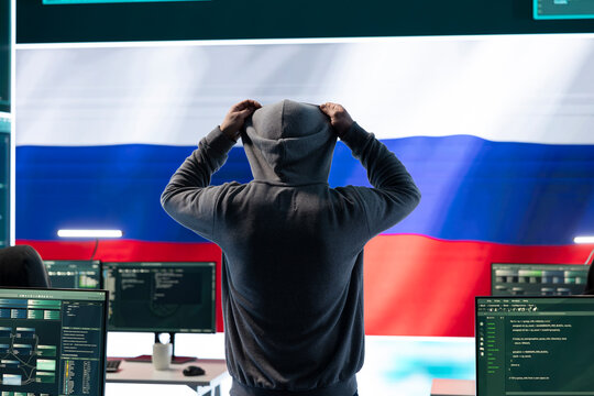 Russian hacker with a hood installing panic by misconception and manipulation, working in governmental cyber operations room. Impact of fake news and ideology propaganda in a hybrid war.