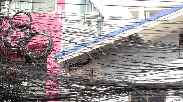 A tangled mess of wires and cables hanging from a building. The wires are black and appear to be in disarray