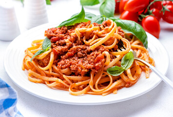 Prepared spaghetti in bolognese sauce or pasta with minced meat and tomatoes decorated green basil, white table background, top view