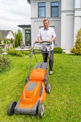 Fototapeta premium An elderly man trims his vibrant lawn with a mower beside his contemporary home