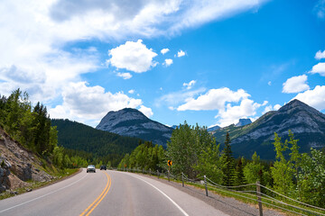 Beautiful view from a car on the Rocky Mountains in Banff National Park in Alberta. Panorama of a road in the mountains past a coniferous forest on a sunny day in summer.