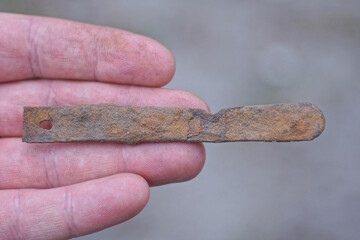 one brown iron small rusty plate lies on the palm of a hand on a gray background