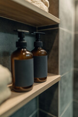 Image of hair and body wash products with a black blank label on them, dispenser on a shelf in a shower room