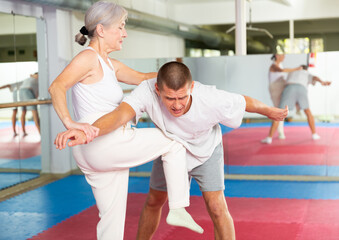 Senior woman learning knee strike move during self-defense training.