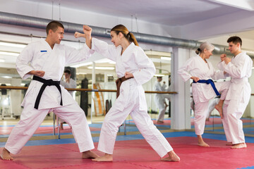 Focused young woman in traditional white kimono sparring with male partner during martial arts...