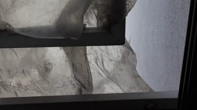 Una toma de cerca de una ventana de un hogar con una bolsa vieja de pl&aacute;stico y sucia movi&eacute;ndose lentamente por el viento