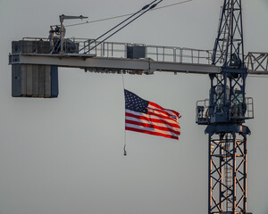 United States flag gracefully flying, back lit by setting sun and hanging from crane on a construction site.
