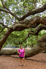 Young woman posing in front of Angel Oak Tree, largest live oak east of the Mississippi river and tourist attraction to Charleston, South Carolina