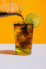 Coffee being poured on glass of lemonade with slice of lime on vibrant yellow background