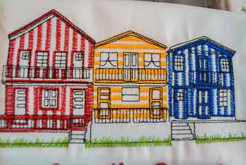 Detailed embroidery of three vibrant Costa Nova beach houses in Aveiro, Portugal. Features red,...