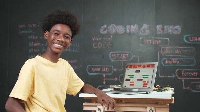 Smart african boy use laptop to code program and turn around to wave hand. Cute high school stident coding engineering prompt or program system at blackboard in STEM technology classroom. Edification