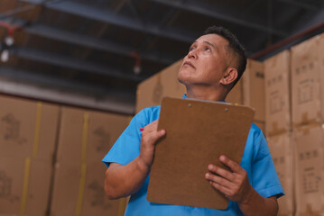 An asian warehouse supervisor suspicious on the count or quality of delivered or stock inventory at the storage depot. Boxes of product in the background.