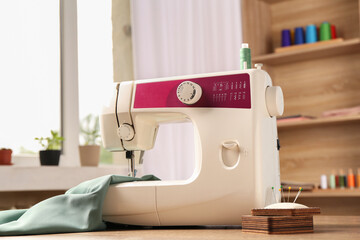 White sewing machine, color fabric and pin cushion with needles on wooden table indoors
