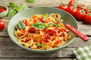 Delicious pasta with tomato sauce, basil and fork in bowl on wooden table, closeup