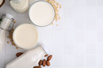 Different types of vegan milk and ingredients on white tiled table, flat lay. Space for text