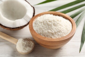 Fresh coconut flour in bowl, spoon, palm leaf and nut on white wooden table, closeup
