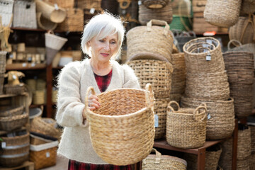 Mature female designer choosing decorative handmade wickerwork for interior in store