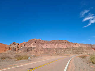 Paved highway in the desert with mountains of sedimentary rocks in the background