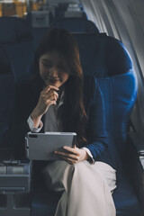 Young Asian executive excels in first class, multitasking with digital tablet, laptop and...