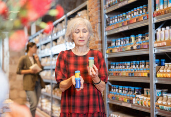 Elderly woman chooses bottle of colored paint for coloring in shop