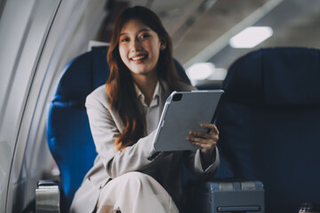 Joyful asian woman sits in the airplane and using tablet while go to travel