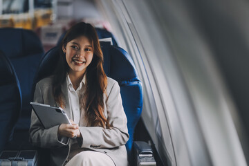 Joyful asian woman sits in the airplane and using tablet while go to travel