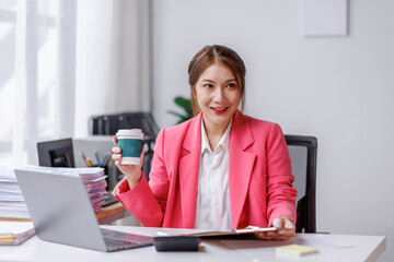 Business asian woman investment consultant analyzing company annual financial report balance sheet statement work and hold cup of coffee with documents graphs.business, market, office, tax.