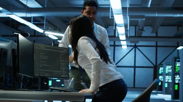 Team of programmers in high tech data center troubleshooting issues using tablet. Teamworking colleagues in server farm using device, establishing performance benchmarks, camera A