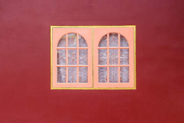 Closed pink wood window with yellow border and mirror curved steel inside on red concrete wall background