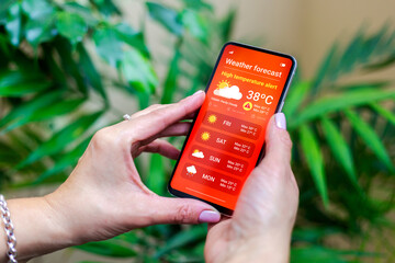 High Temperature Alert. Woman outdoors checking the weather forecast on an app on her mobile phone....