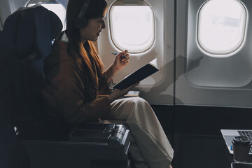 A young Asian woman, seated as an airplane passenger, contemplates dollar bills, reflecting on...