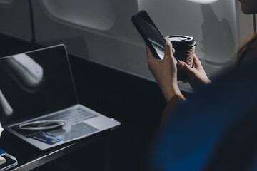 A young Asian woman, seated as an airplane passenger, contemplates dollar bills, reflecting on...