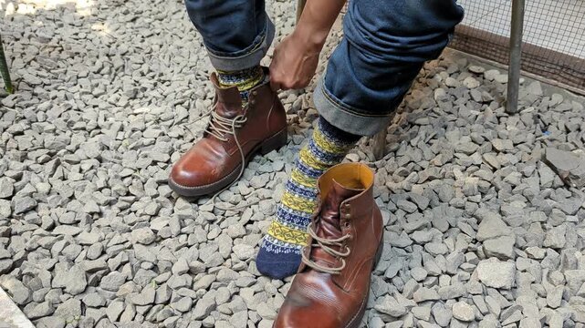 Man in jeans putting on and tying red leather boots shoes, in rock floor, rugged, stock video, 4K.